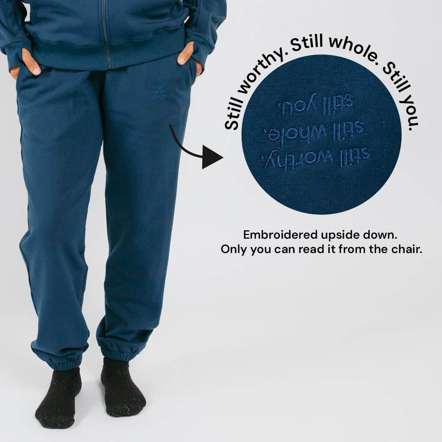 Blue sweatpants with embroidered text on the back pocket visible only when seated.