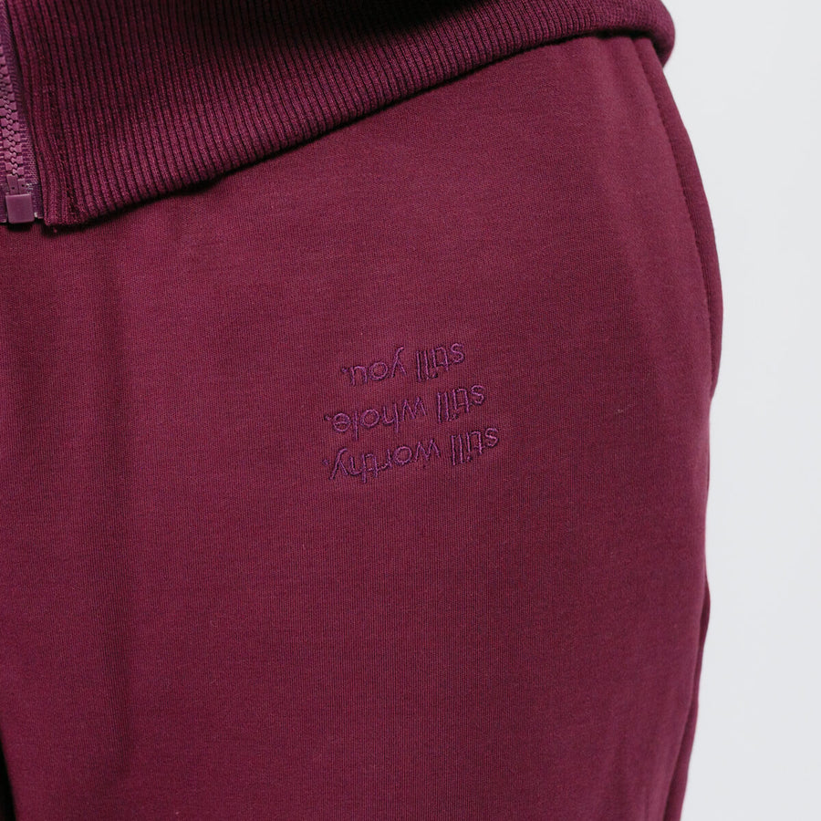 Burgundy sweatpants with ribbed waistband and embroidered text detail on the thigh.