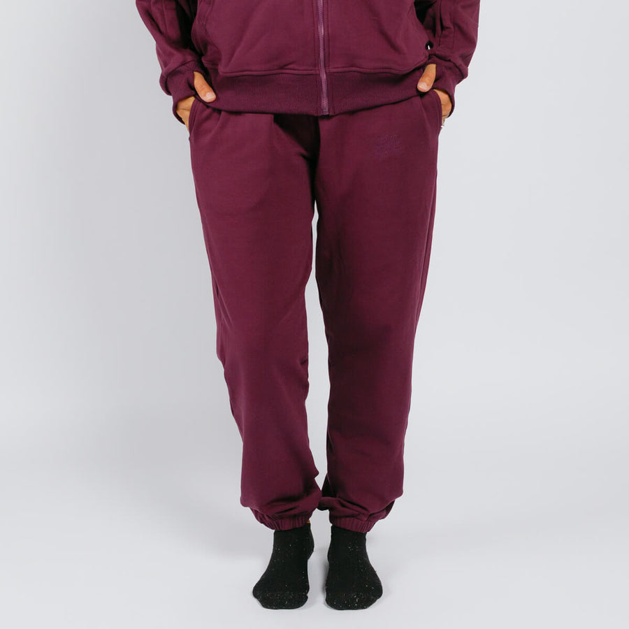 Person wearing maroon sweatpants with cuffed ankles and black socks against a white background.