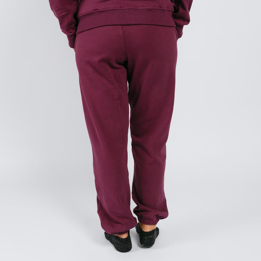Person wearing maroon sweatpants viewed from behind, standing against white background.