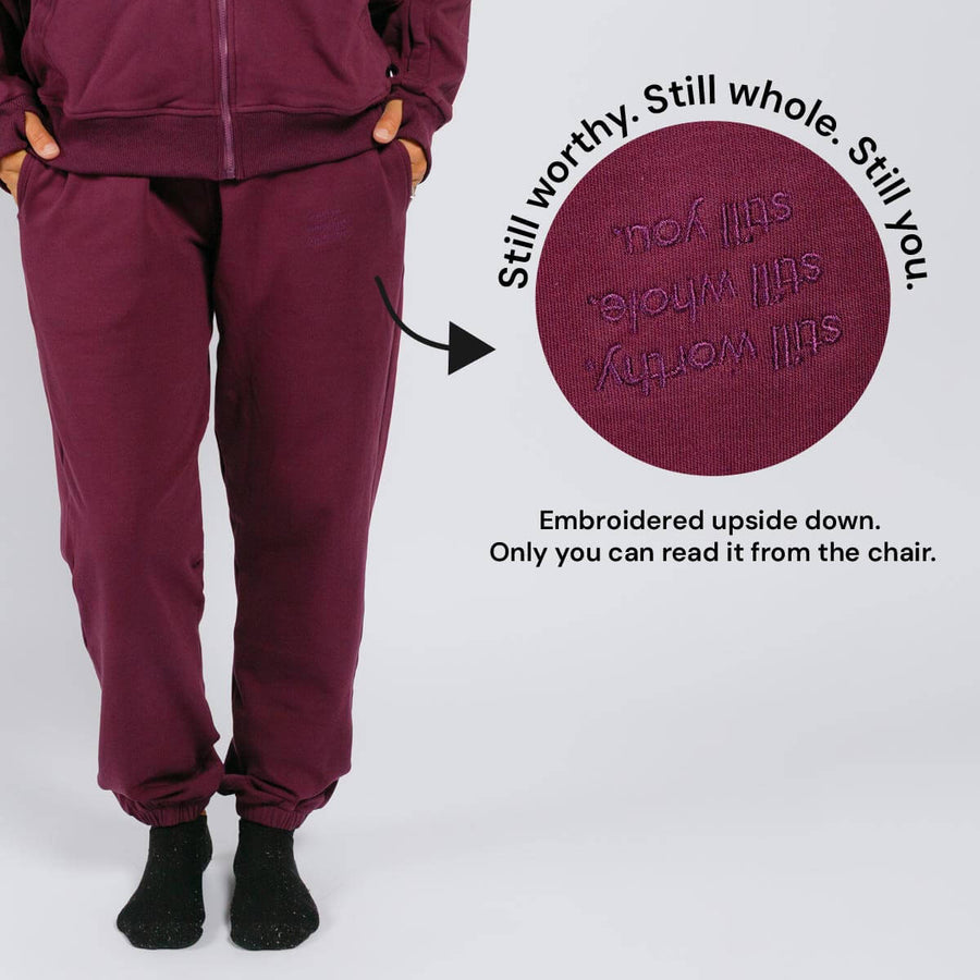 Maroon sweatpants with upside-down embroidered text on the thigh visible only when seated.