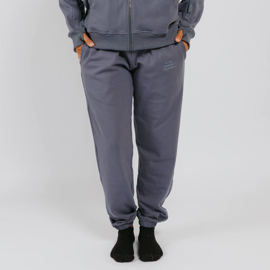 Person wearing gray sweatpants with orange thumb holes and black socks against white background.
