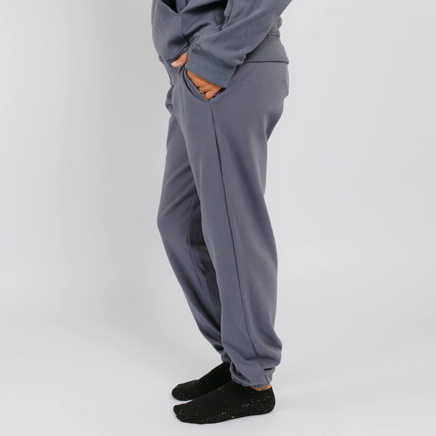 Person wearing slate blue sweatpants with orange pocket lining and black socks against white background.