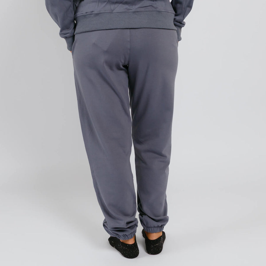 Person wearing slate blue sweatpants with cuffed ankles, viewed from behind against a white background.