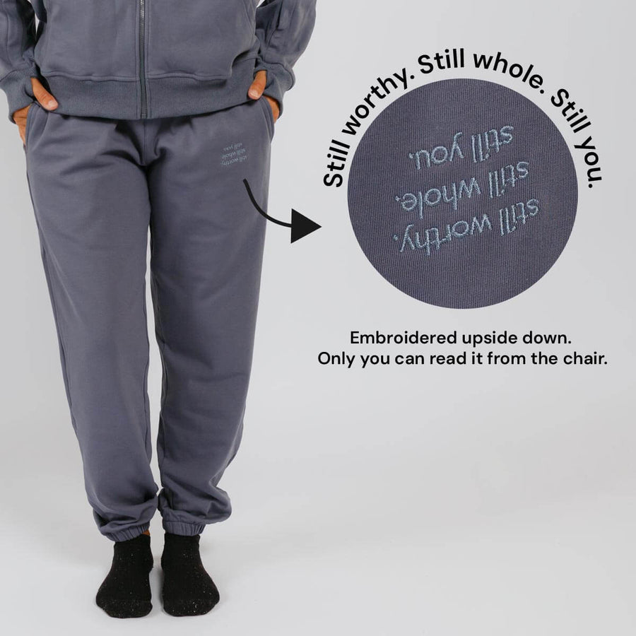 Slate blue sweatpants with upside-down embroidered text on the back pocket visible only when seated.