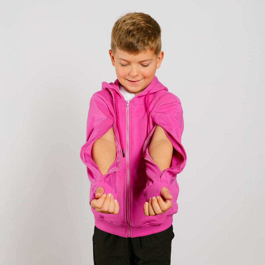 Young boy wearing a bright pink zip-up hoodie with cutout sleeves over black pants. #NEW Child wearing a pink hoodie with cut-out sleeves on a light gray background