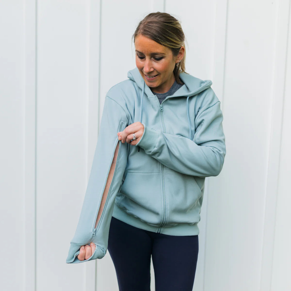 Woman demonstrating IV-accessible zip hoodie sleeve design for medical treatment comfort.