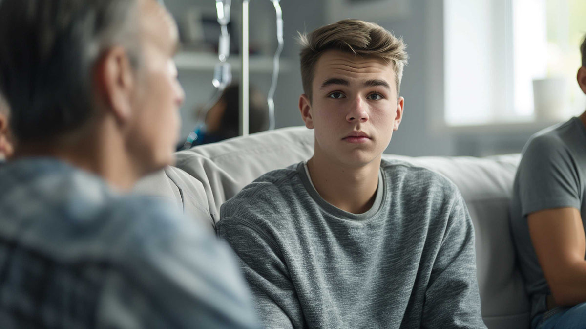 Young man in hospital gown sits listening during what appears to be a support group or counseling session.