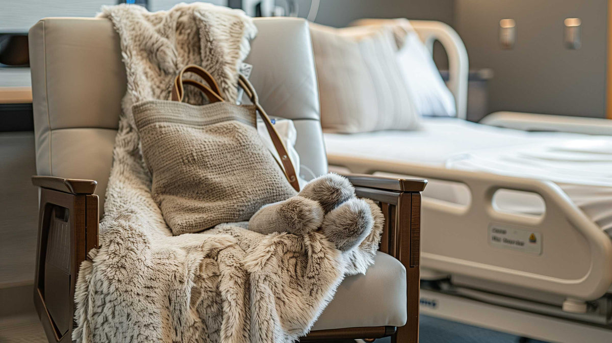 Cozy blankets and adaptive clothing arranged on a hospital chair beside a medical bed.