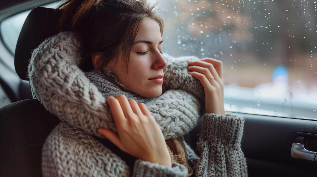 Woman in cozy winter clothing gazes out rainy car window during travel.