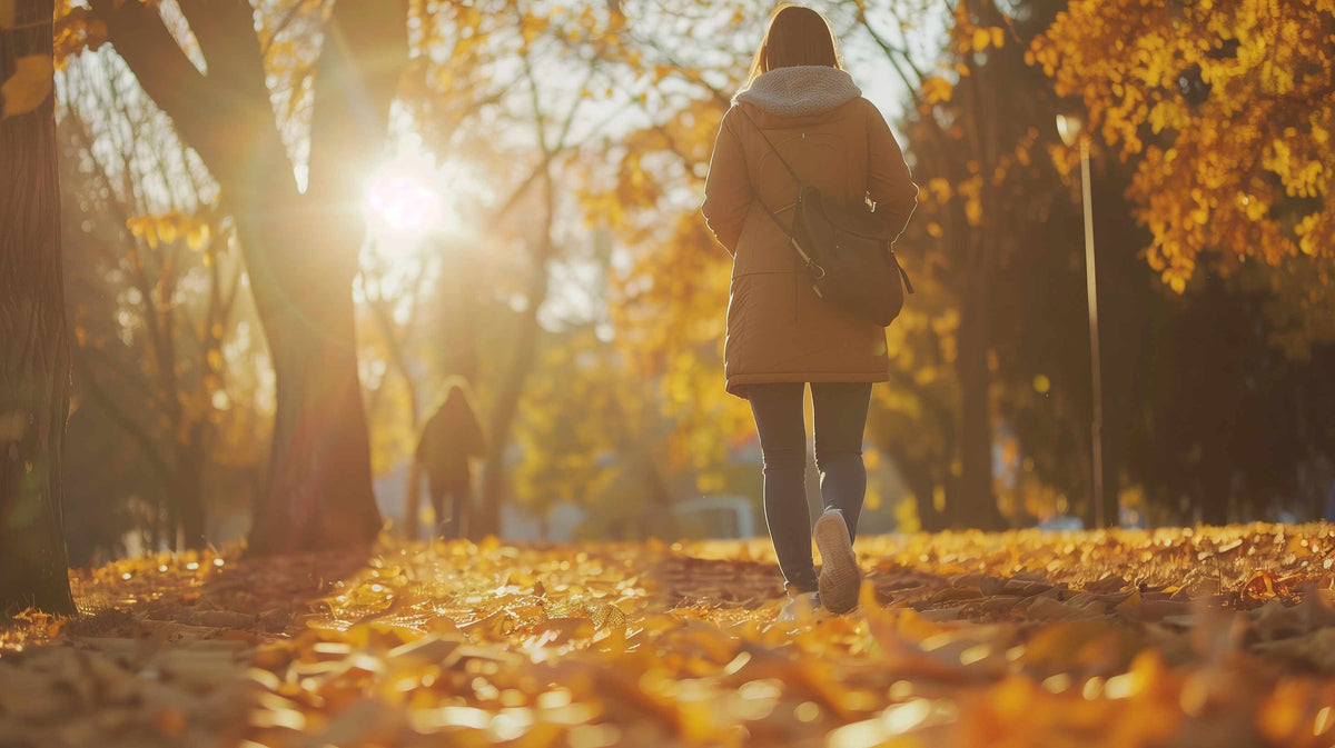 Person jogging alone on a tree-lined autumn path covered in golden fallen leaves.