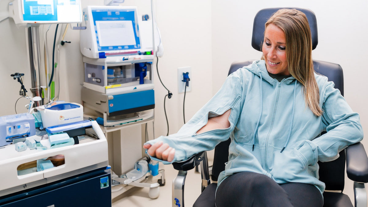 Woman in light blue adaptive hoodie receives medical treatment in clinical setting with specialized equipment.