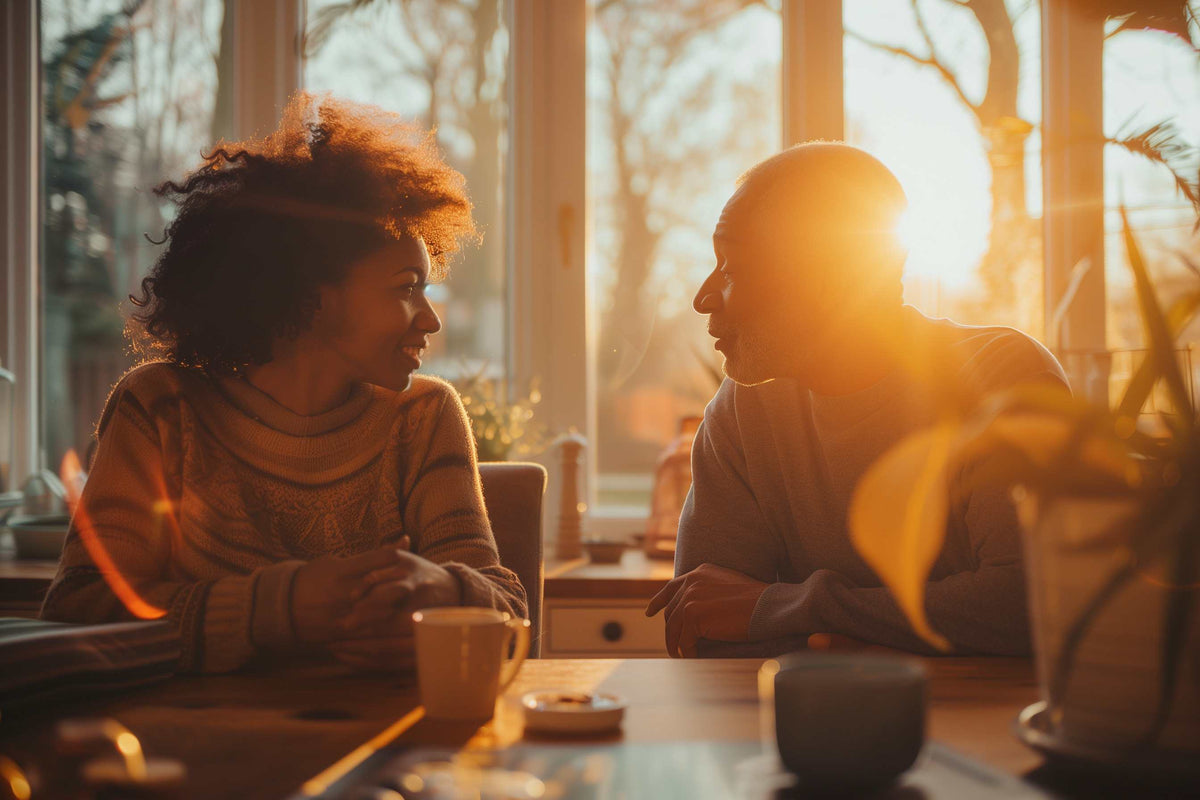 A women who is a caregiver to a man, having a conversation at sunrise at a kitchen table.