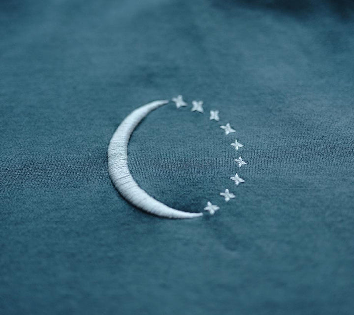 The crescent moon embroidered in silver thread, with stars tracing the rest of the circle