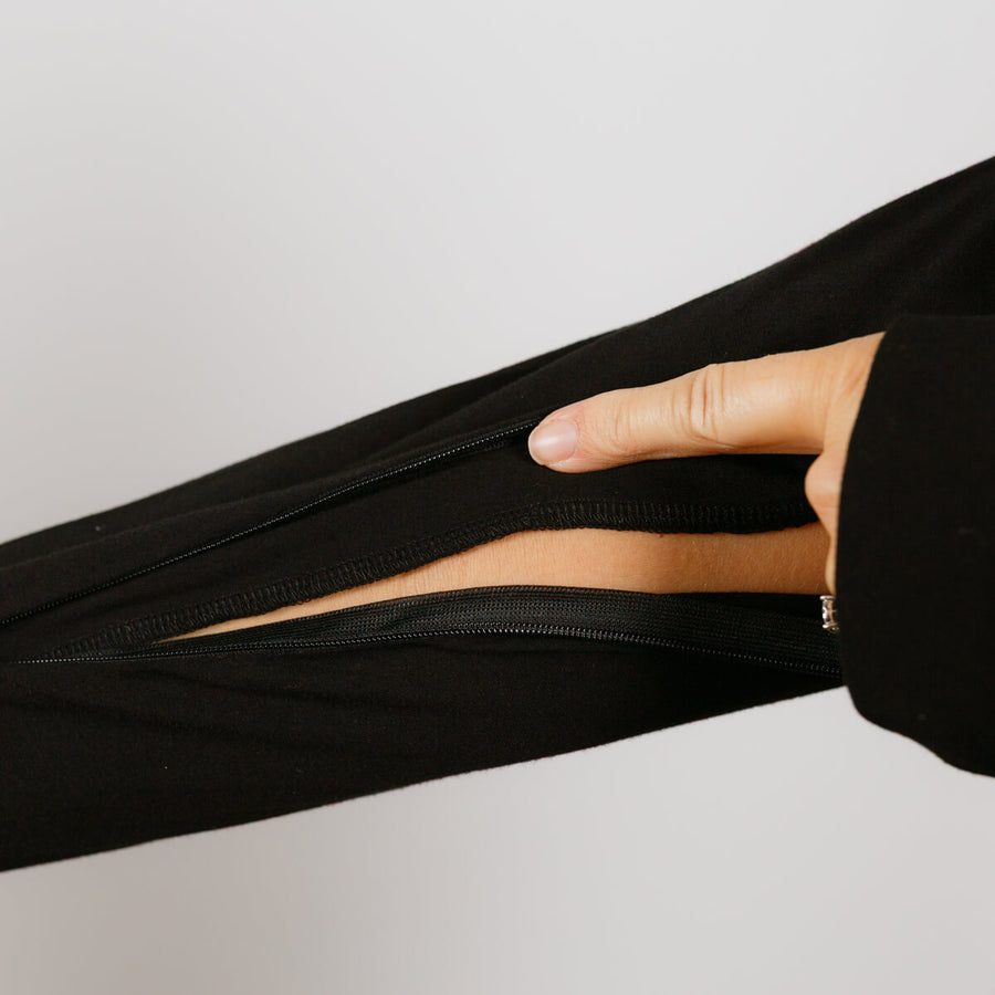 Person wearing black bamboo IV zip hoodie with left sleeve zipper open revealing arm access port.