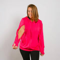 Woman wearing a bright pink zip-up hoodie with cutout sleeves over black pants, smiling downward. #NEW Woman wearing a bright pink hoodie with cut-out sleeves on a plain background | Model is 5'3" 130lbs wearing size S