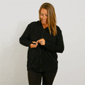 Woman wearing a black zip hoodie, smiling while zipping the front closure.