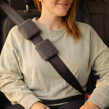 Woman wearing cream sweatshirt with gray padded shoulder belt covers in car seat. #NEW #NEW