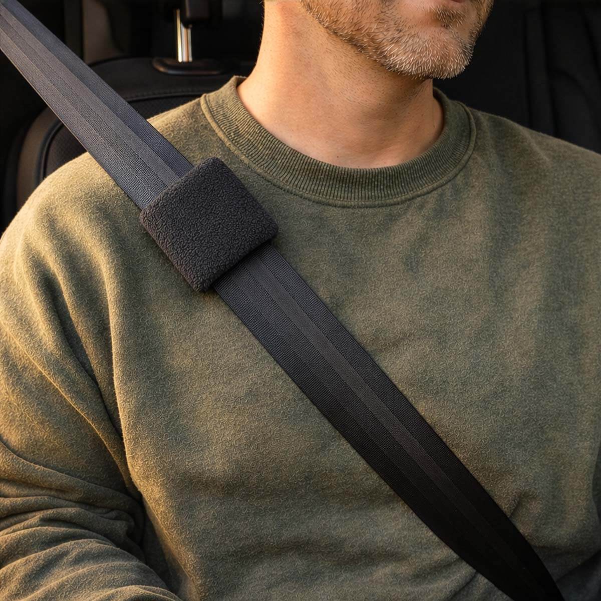 Man wearing olive sweatshirt with gray padded seatbelt port cover across chest.