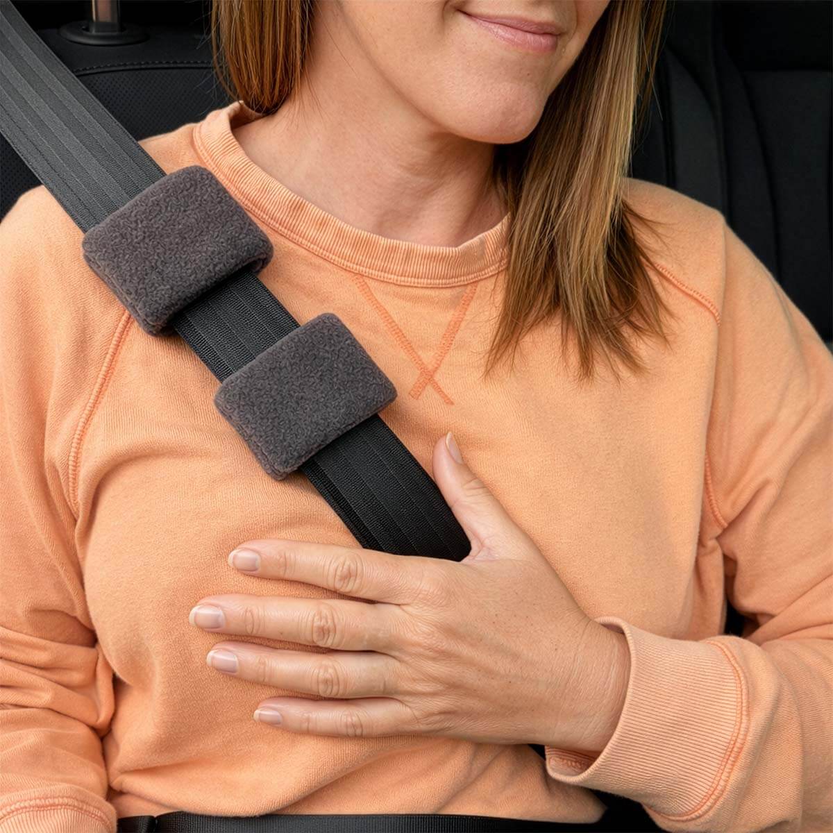 Woman wearing peach sweatshirt with gray padded seatbelt port covers.