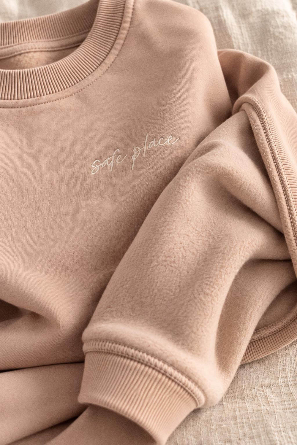 Close-up of the crewneck's soft brushed lining and ribbed cuff, with "safe place" embroidered on the chest.