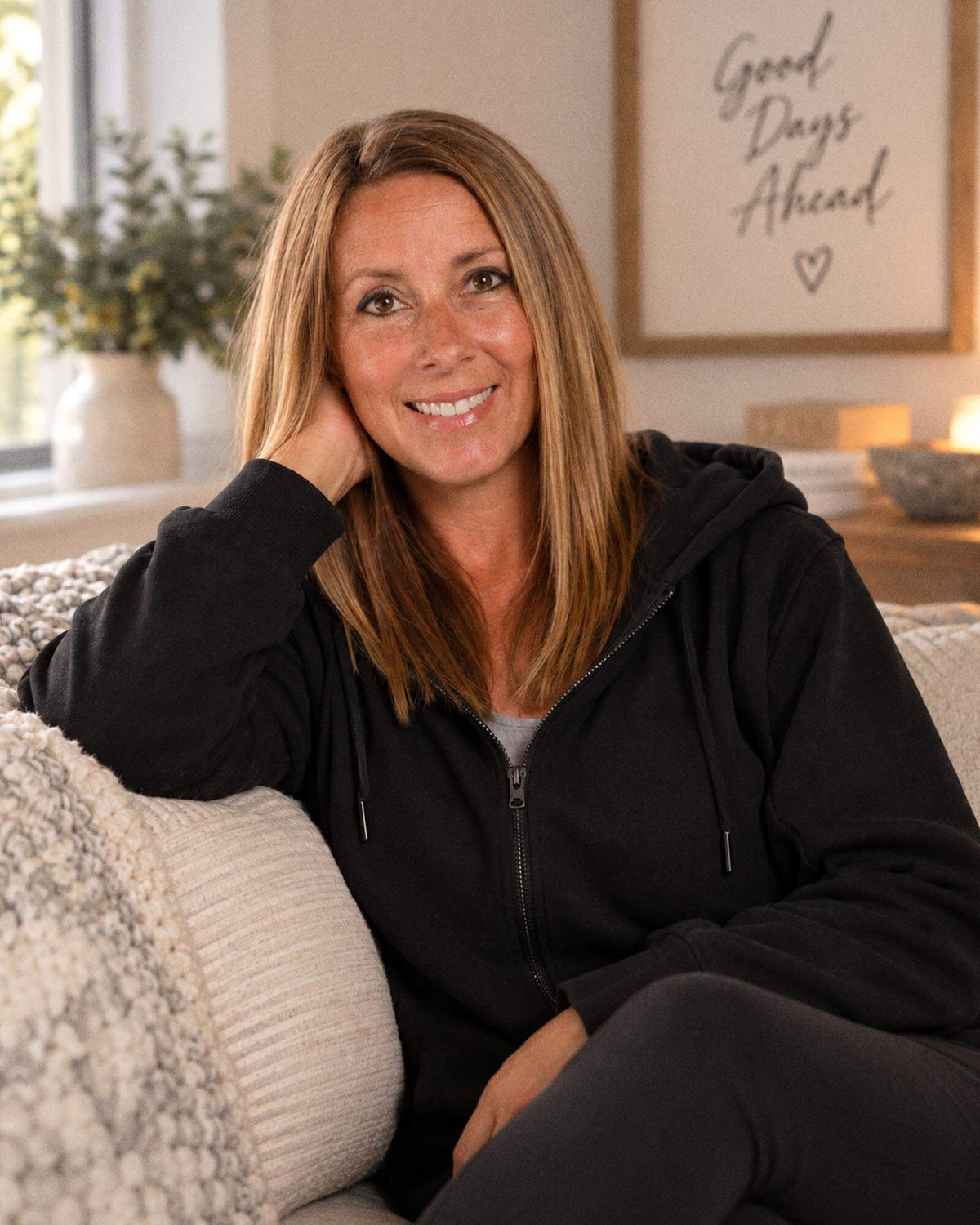BeWell founder, Amanda, sitting on a cozy couch with her head resting on her face, wearing a black IV Zip Hoodie.