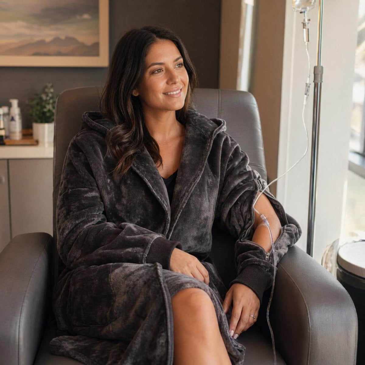 Woman in dark velvet robe seated in modern chair, smiling toward window in neutral-toned room.