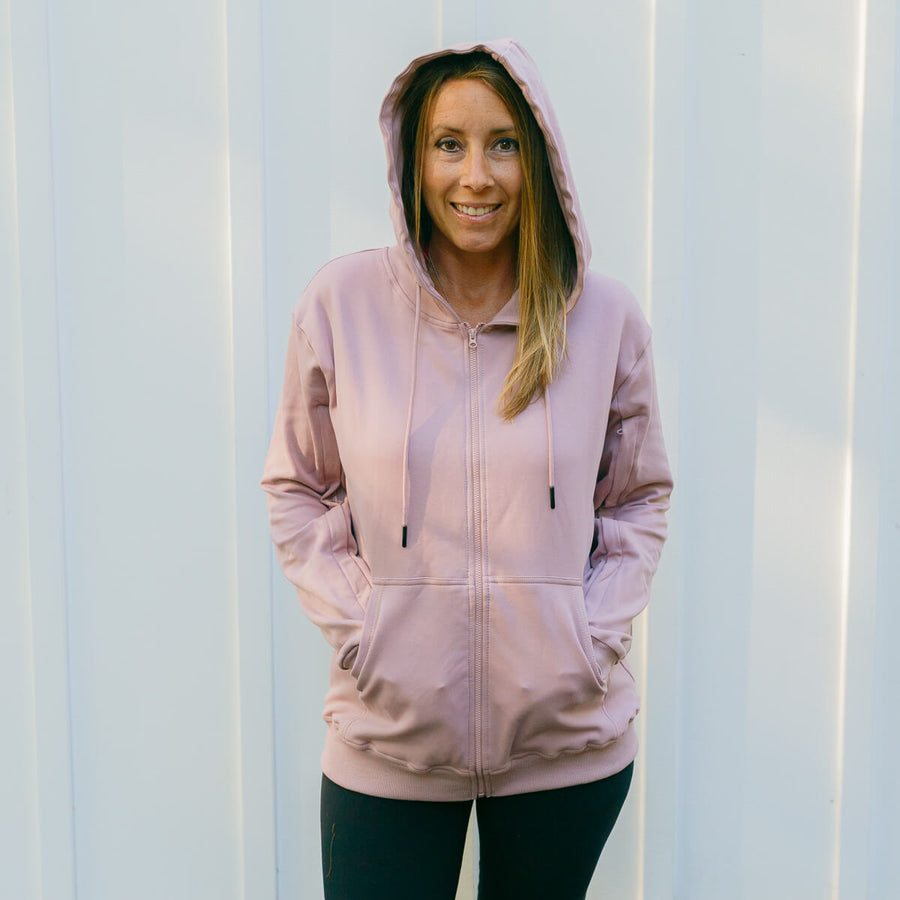 Woman wearing lavender IV zip hoodie with front zipper, standing against white striped background.
