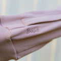 Close-up of light pink IV zip hoodie showing embroidered BeWell logo on sleeve.