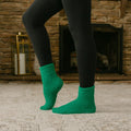 Person wearing black leggings and green rest day socks standing by fireplace.