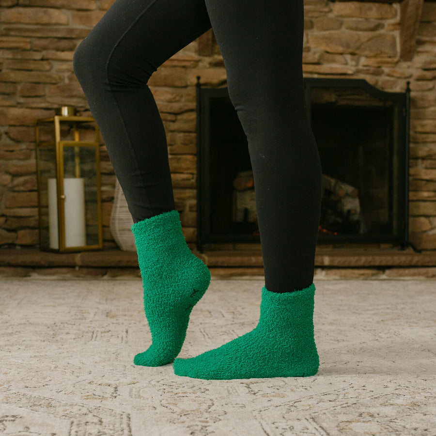 Person wearing black leggings and green rest day socks standing by fireplace.