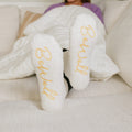Woman wearing white Rest Day socks with gold text, feet up on couch.