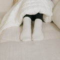 Person wearing white Rest Day socks while bundled under white bedding in bed.