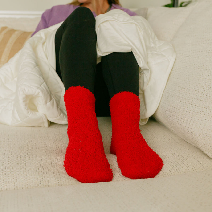 Woman wearing bright red rest day socks while relaxing on couch with blanket.