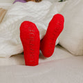 Close-up of red Rest Day Socks displayed on neutral bedding with embroidered text detail.