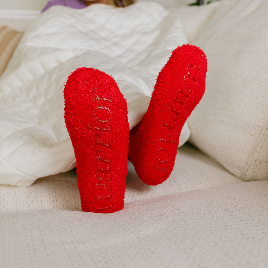 Close-up of red Rest Day Socks displayed on neutral bedding with embroidered text detail.