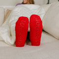 Woman sitting on couch wearing bright red fluffy socks with grip sole detail.