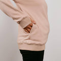 Beige crewneck sweatshirt with thumb holes in sleeves, worn over black pants.