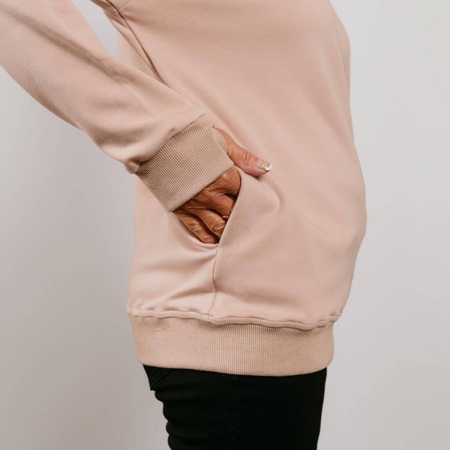 Beige crewneck sweatshirt with thumb holes in sleeves, worn over black pants.