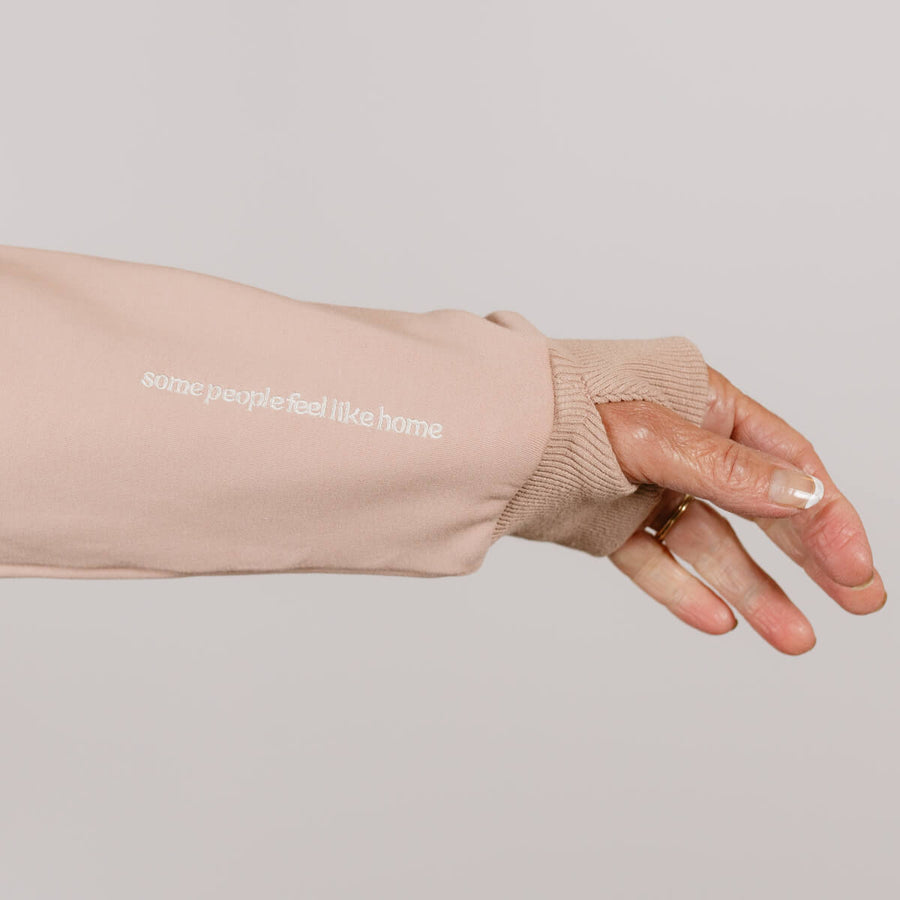 Person wearing a beige crewneck sweatshirt with white text on the sleeve, displaying their hand and manicured nails.
