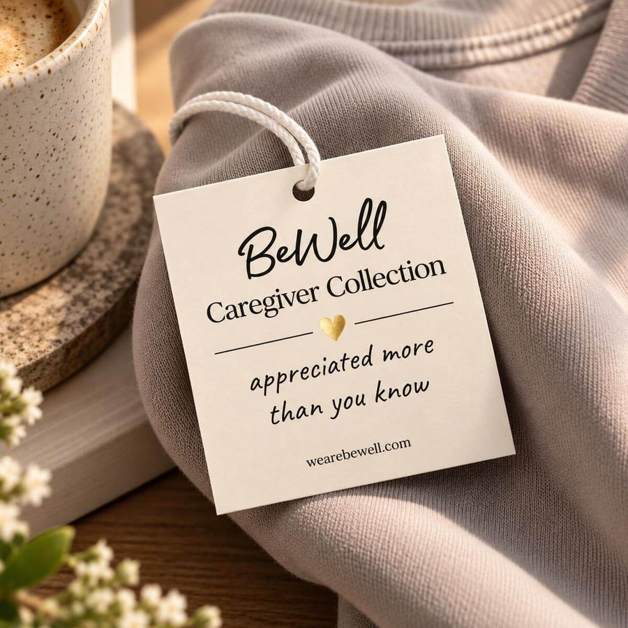 Cream tag attached to folded gray crewneck sweatshirt beside coffee mug and white flowers.