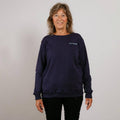 Woman wearing a dark navy crewneck sweatshirt with long sleeves standing against a light background. | Model is 5'3" 139lbs wearing size S