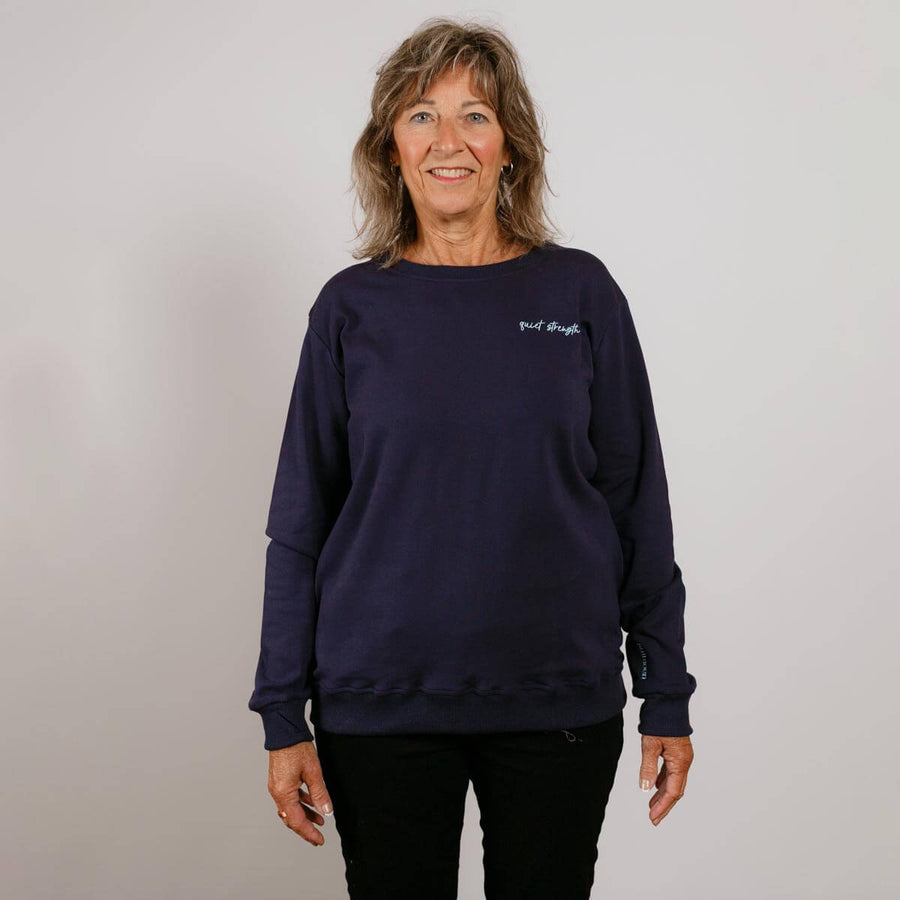 Woman wearing a dark navy crewneck sweatshirt with long sleeves standing against a light background.