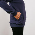 Person wearing navy crewneck sweatshirt with hand in front pocket, black pants visible below.