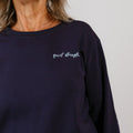 Navy crewneck sweatshirt with "quiet strength" embroidered in white script on the chest.
