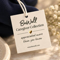 A cream-colored gift tag with handwritten-style text hangs from a dark navy crewneck sweater surrounded by baby's breath flowers.