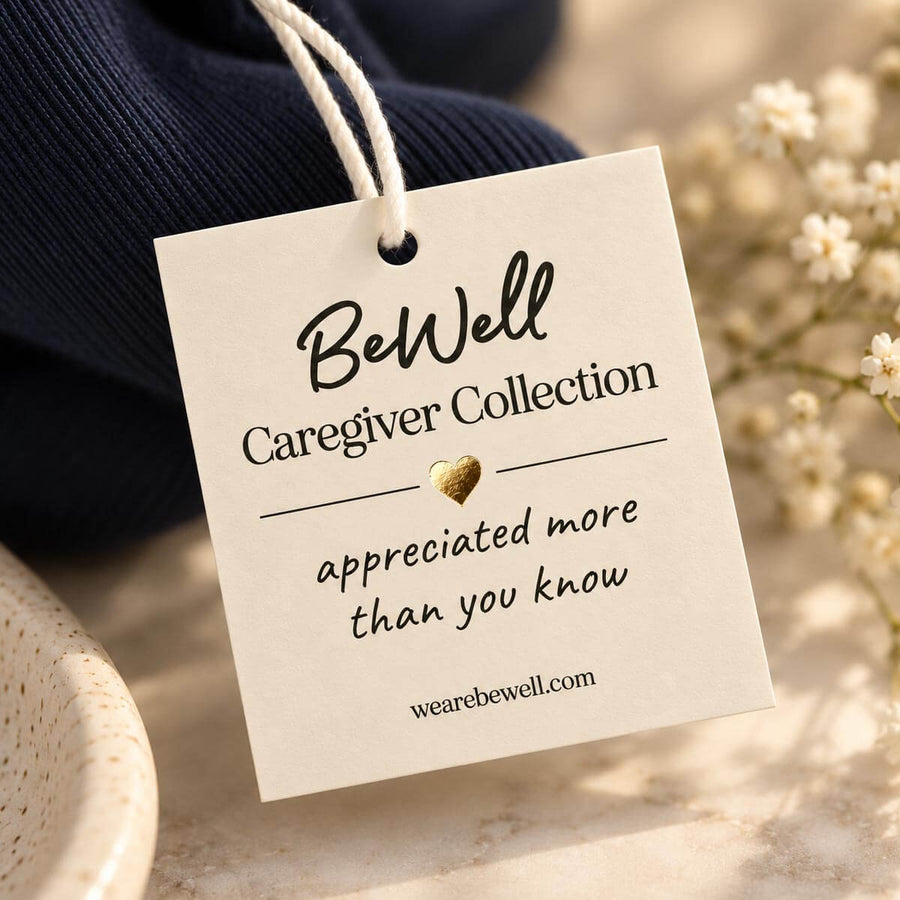 A cream-colored gift tag with handwritten-style text hangs from a dark navy crewneck sweater surrounded by baby's breath flowers.