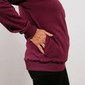 An older person's hand rests in the front pocket of a burgundy crewneck sweatshirt.