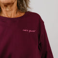 Woman wearing a burgundy crewneck sweatshirt with "care giver" embroidered in cursive lettering.