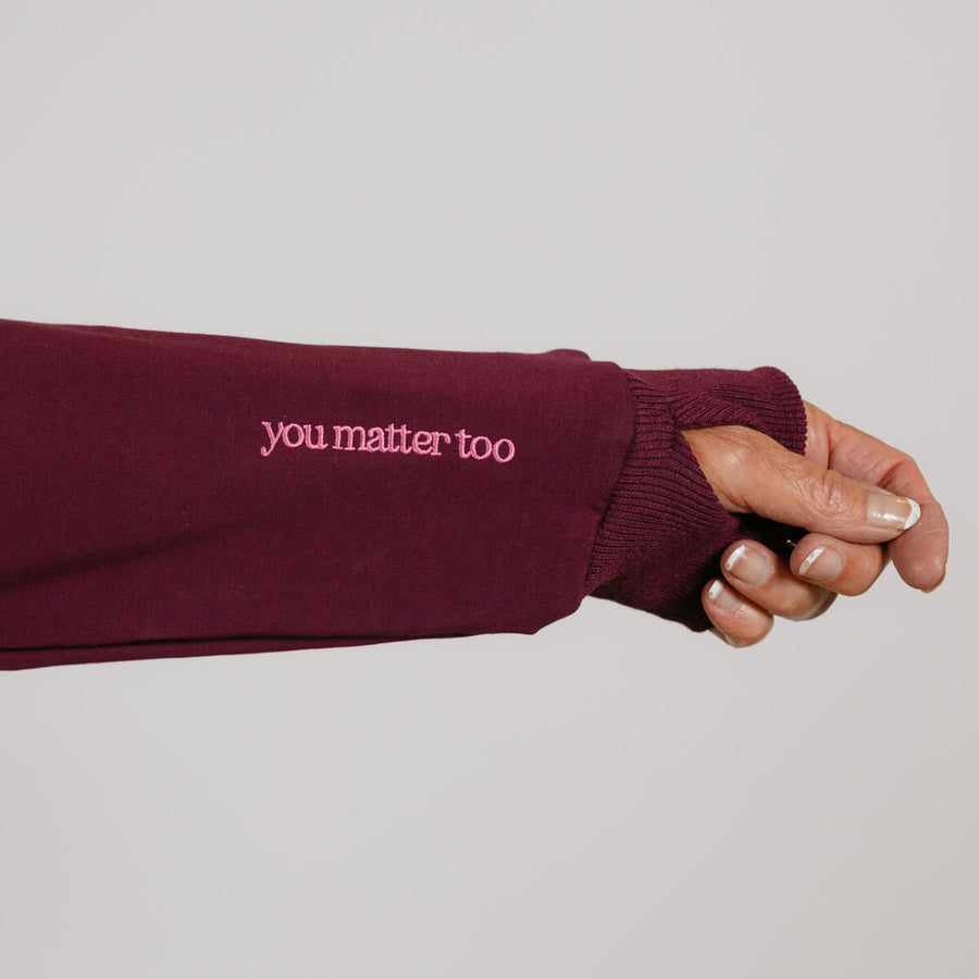 Maroon crewneck sweatshirt with "you matter too" text displayed on the sleeve of an outstretched arm.